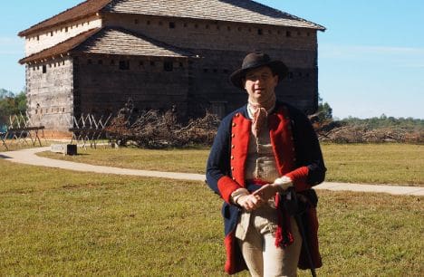 A man in costume standing outside of a barn.